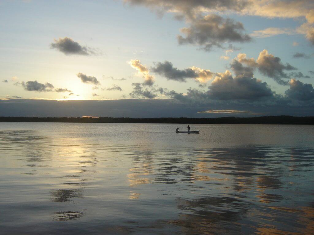 O barco passeia pelas águas calmas enquanto os últimos raios de sol iluminam o rio